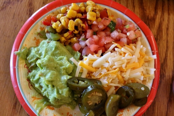 A plate of toppings like guacamole, jalapenos, tomato, and shredded cheese