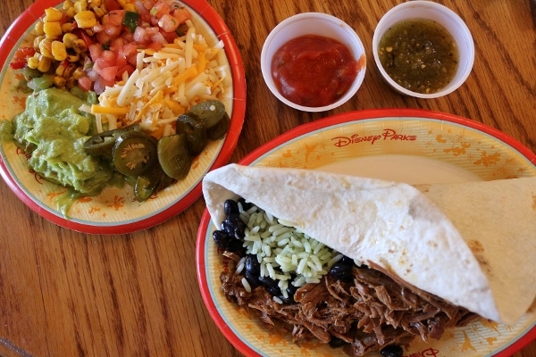 a beef burrito with various toppings on a side plate