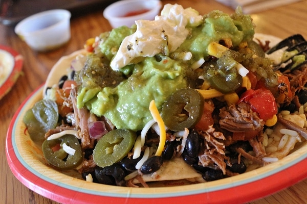 A plate full of Mexican food with jalapenos, cheese, and guacamole on top