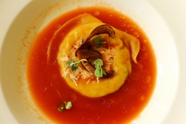 overhead view of a giant ravioli in a tomato broth