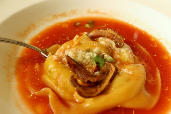 closeup of a large ravioli in a tomato broth