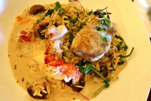 a plate of orzo pasta topped with a fish fillet and lobster tail