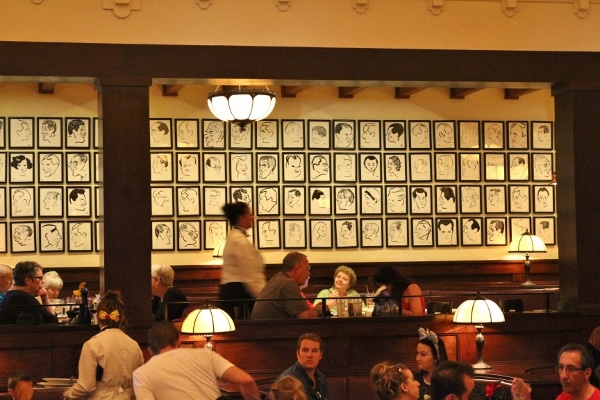 a restaurant dining room filled with people with framed drawings on a distant wall