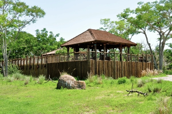 a fenced off area with a thatched roof in the middle of a field