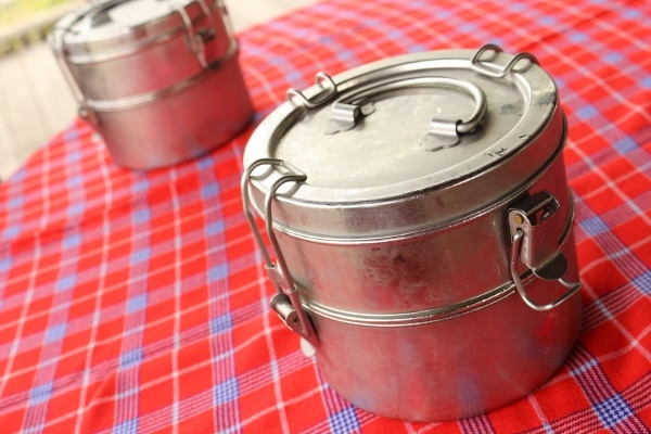 two metal tiffins (food storage containers) on a checkered tablecloth