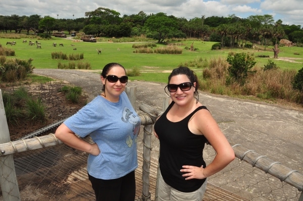 two women posing in front of a large savanna with grass and trees