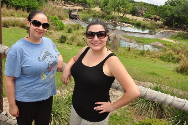 two women posing in front of a large savanna a small body of water