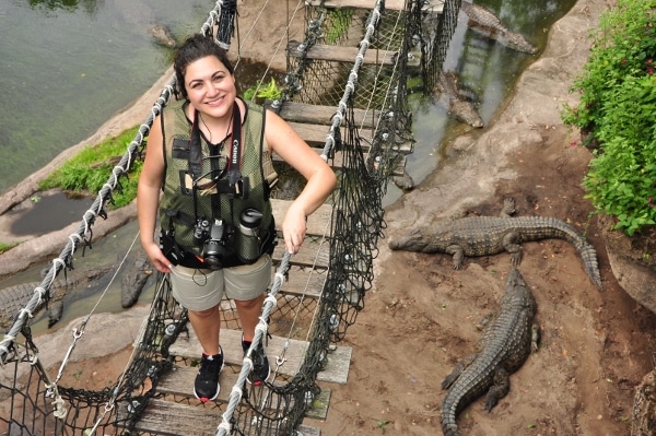 a woman posing on a rope bridge with crocodiles underneath the bridge