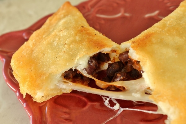 A close up of a cheesy fried empanada broken in half to show the filling