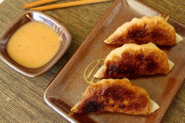 Three pan-fried dumplings on a plate with dipping sauce to the side