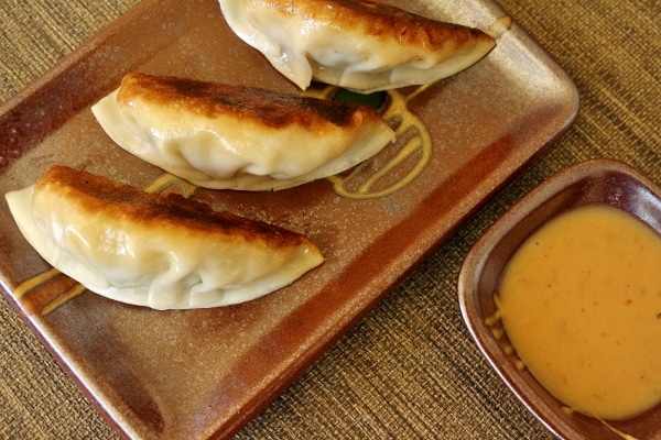 a closeup of fried dumplings on a dark-colored plate with dipping sauce on the side