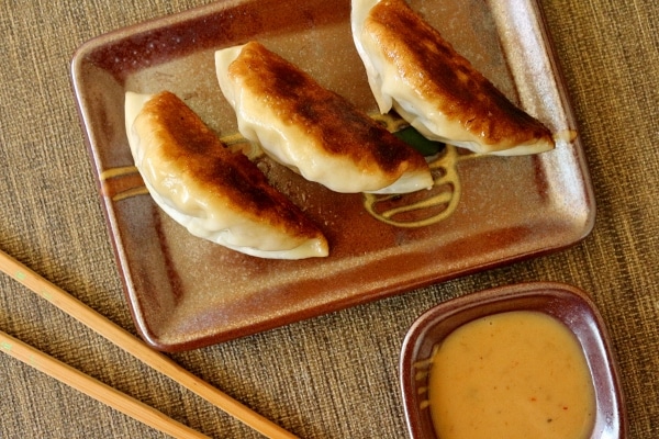 overhead view of pan-fried dumplings on a plate with chopsticks and sauce