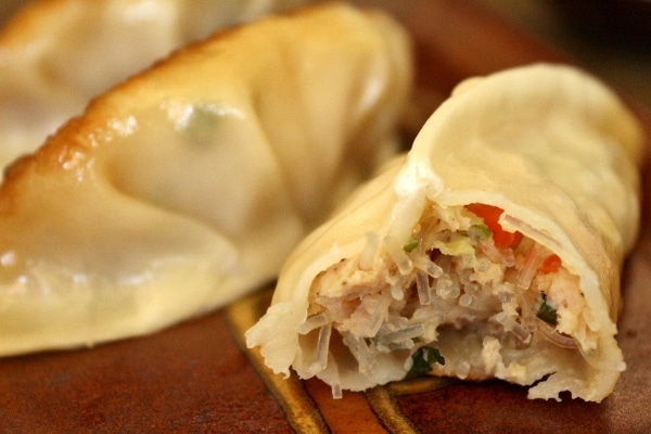 A close up of a half-eaten chicken and thai basil dumpling on a plate