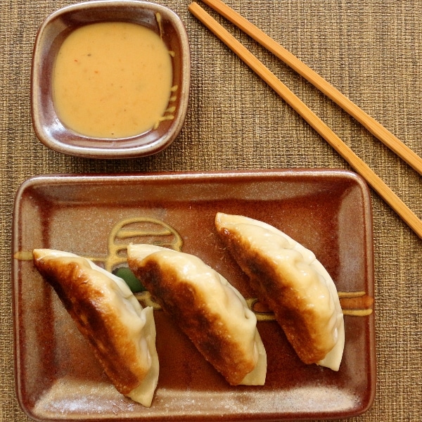 overhead view of three pan-fried dumplings with chopsticks and dipping sauce