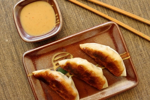 three fried dumplings on a rectangular plate with chopsticks and dipping sauce