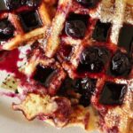 A plate of half-eaten waffles topped with powdered sugar and blueberry syrup.
