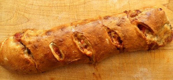a wide view of a baked stromboli with cheese bubbling out of the slits on top