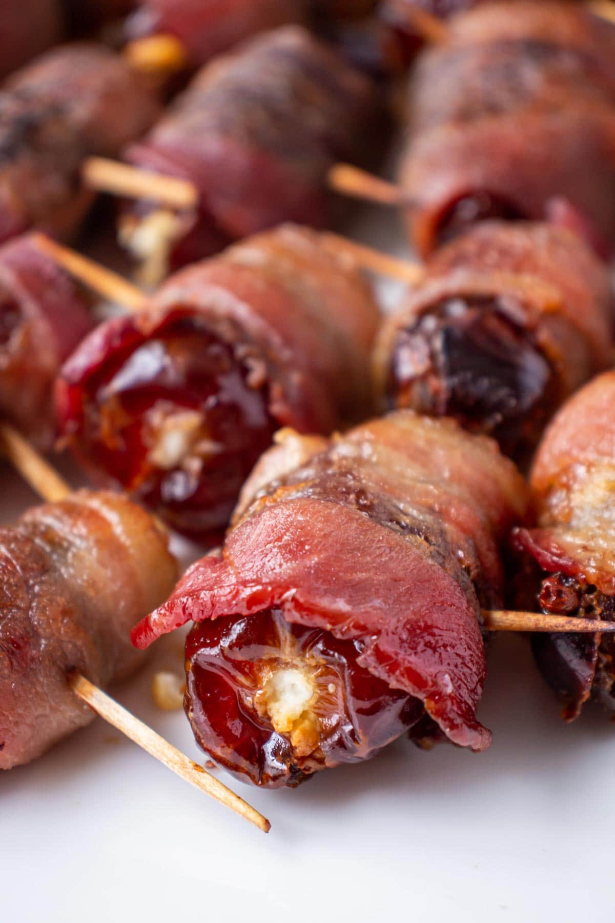 Closeup of Devils on horseback (baked goat cheese stuffed dates) on a white plate.