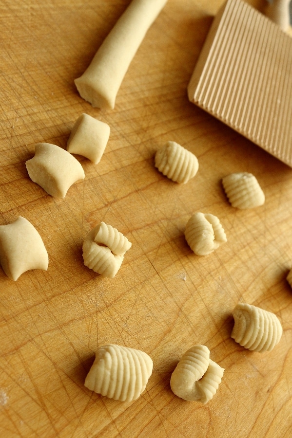 A wooden cutting board with ricotta cavatelli and a gnocchi board on top