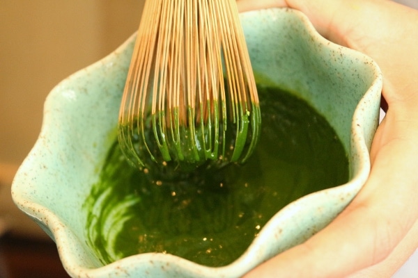 A close up of a bowl of matcha tea with a bamboo whisk