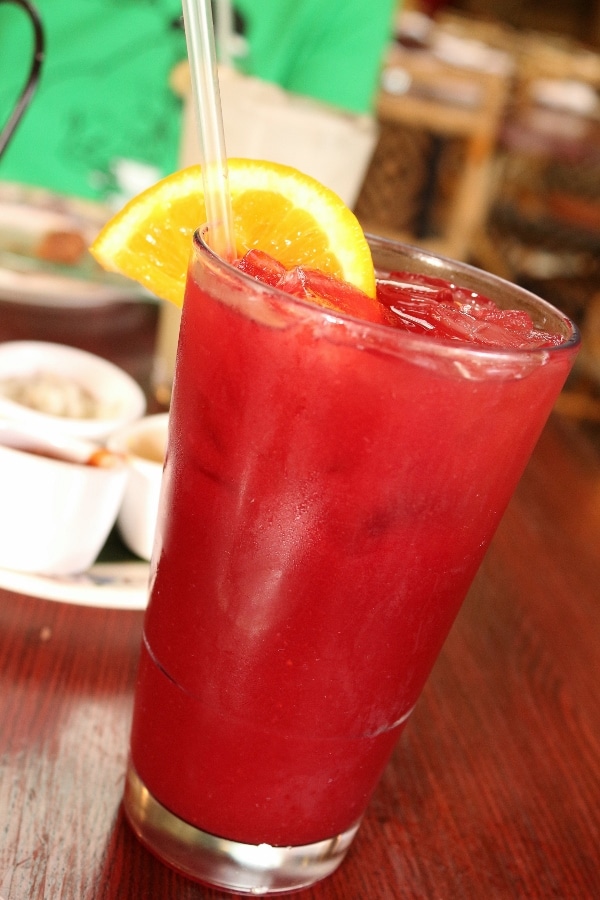 a red drink in a tall glass with an orange slice garnish