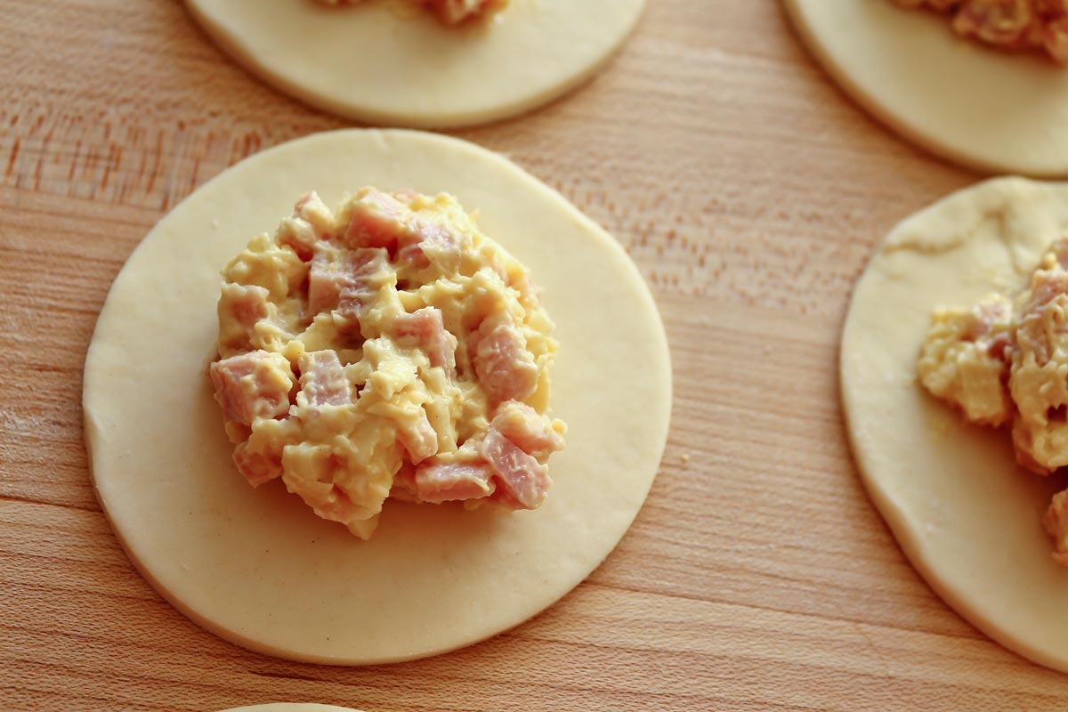 Closeup of dough circles topped with ham and cheese filling on a wooden board.