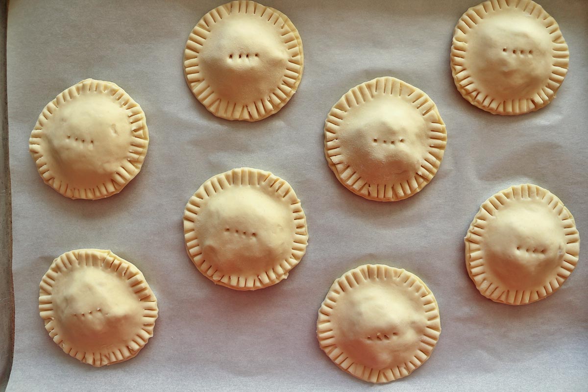 Round unbaked empanadas on a baking sheet.