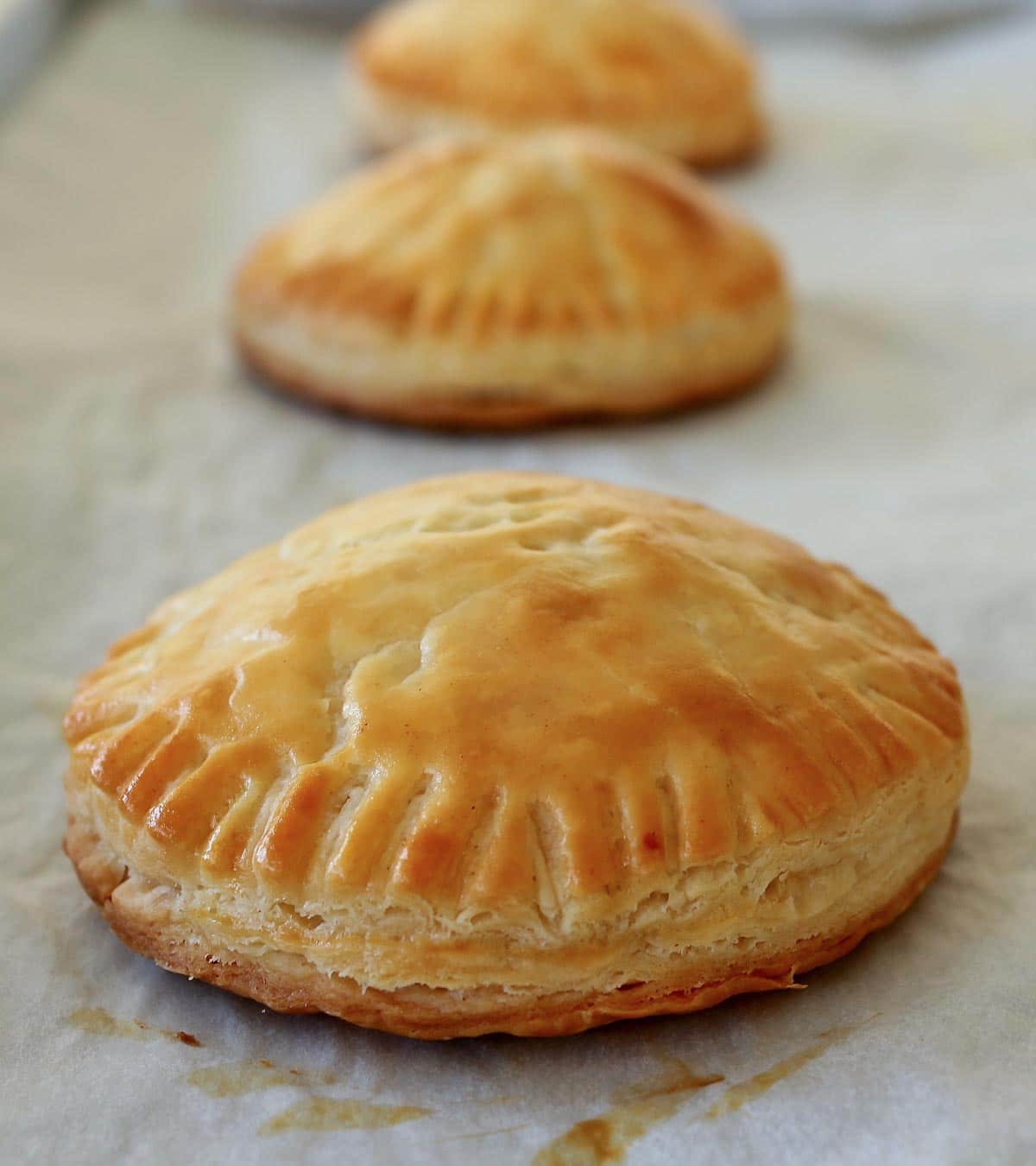 Closeup of a row of round baked empanadas on a baking sheet.