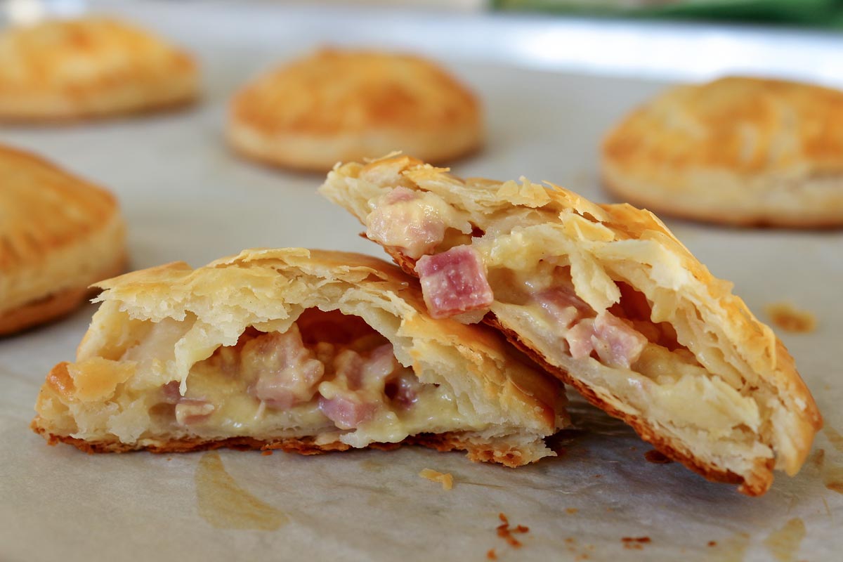 Baked ham and cheese empanadas on a baking sheet with one broken in half.