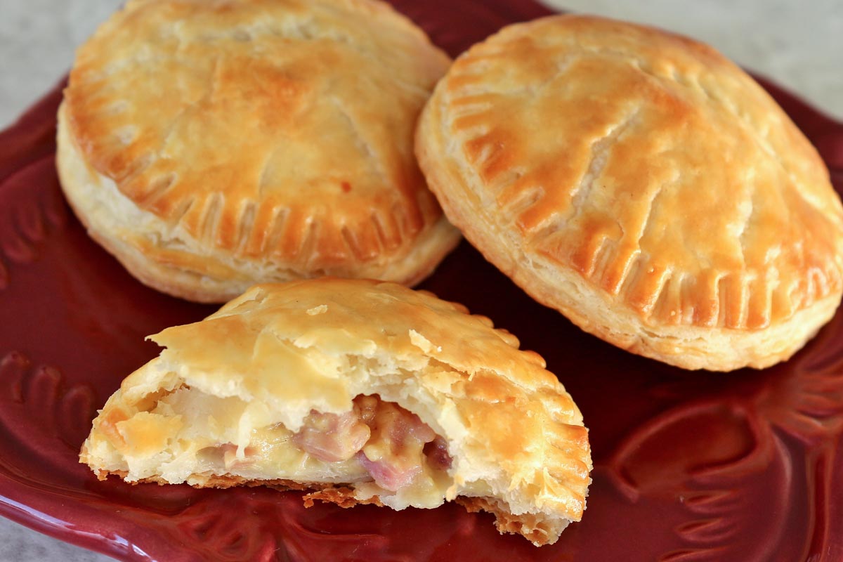 Two and a half round ham and cheese empanadas on a square dark red plate.