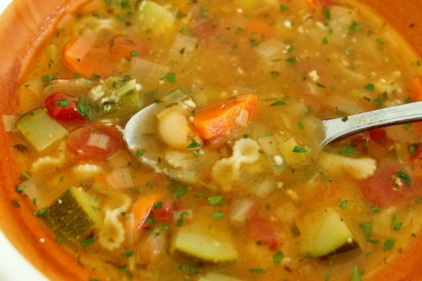 closeup of a bowl of minestrone soup with a spoon scooping some up