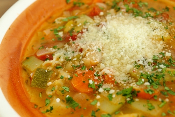 a bowl of minestrone soup with a pile of Parmesan cheese in the center