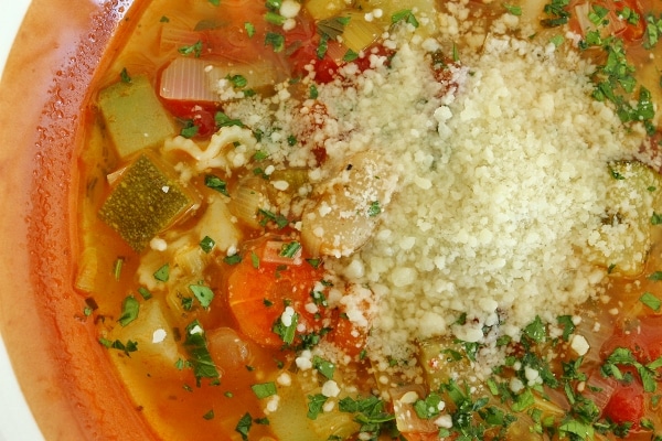 a bowl of minestrone soup with a pile of grated parmesan cheese on top