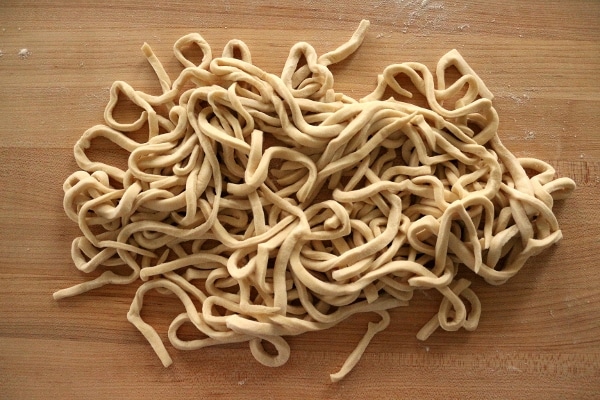 a pile of freshly cut homemade udon noodles on a wooden board
