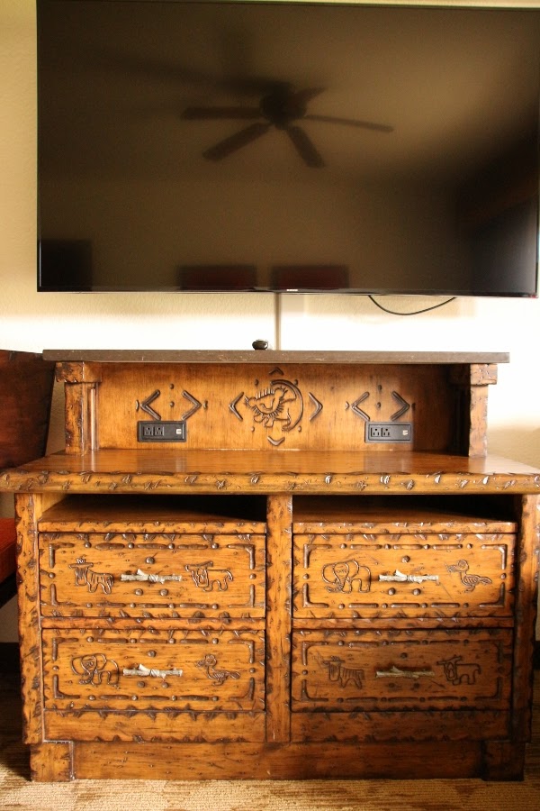 a wooden dresser with animal carvings beneath a flat screen television