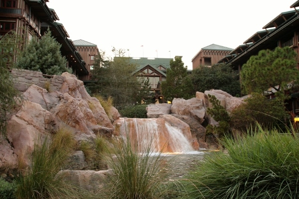 a small waterfall surrounded by rocks and trees with the Wilderness Lodge in the background