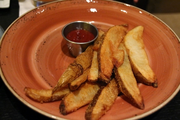 potatoes wedges on an orange plate with a dipping cup of ketchup