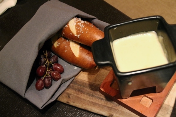 a small black dish of cheese fondue served with pretzel bread sticks and grapes