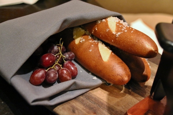 closeup of pretzel bread sticks and red grapes on a wooden board