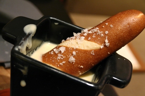 a pretzel bread stick dipping into cheese fondue