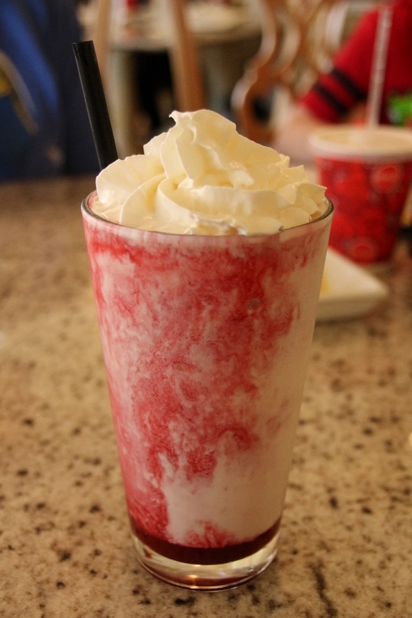 a blended strawberry drink in a tall glass with whipped cream on top