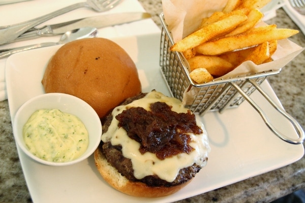 a burger with its top bun off, served with a small basket of fries