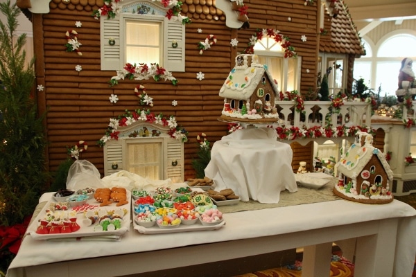 a wide view of a gingerbread house display with trays of candy for decorating