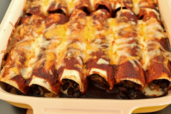 a closeup of enchiladas with dark red sauce and cheese in a casserole dish