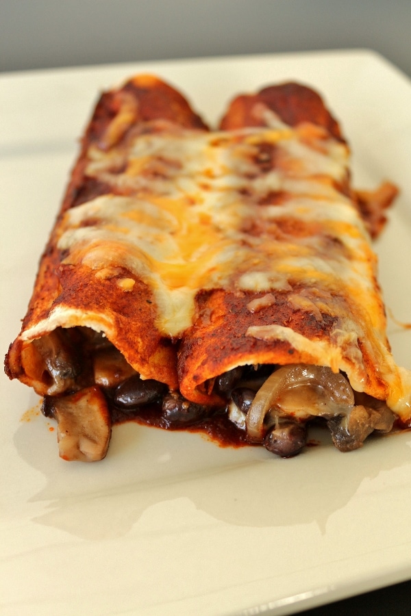 a side view of vegetarian enchiladas with red sauce and melted cheese on a plate