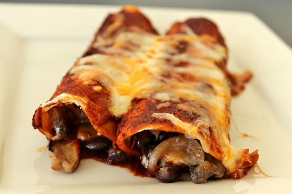 a closeup of two enchiladas with mushroom and black bean filling, and red sauce