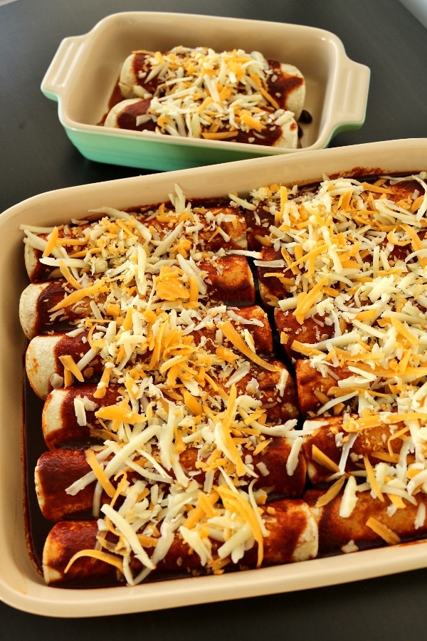 unbaked casserole dishes filled with enchiladas topped with cheese