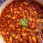 Cape Malay chicken curry garnished with cilantro in an enameled cast iron pan.