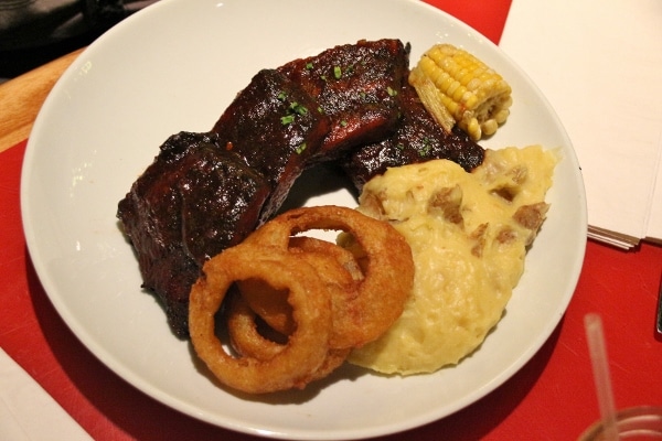 A plate of pork ribs with mashed potatoes, onion rings, and corn on the cob