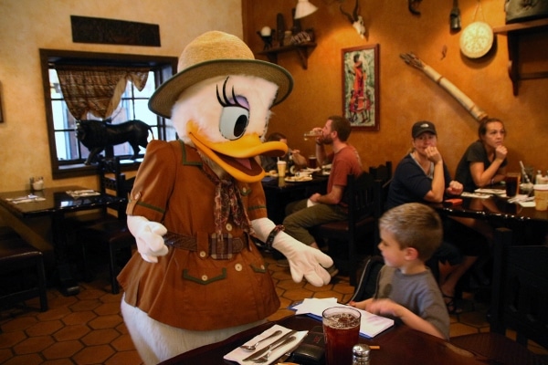 A young boy sitting at a table next to Daisy Duck